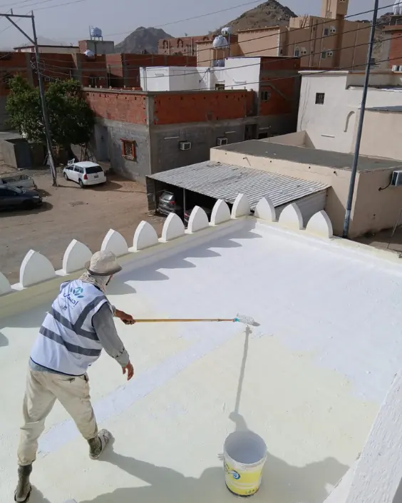 فني يدهن طبقة العزل المائي البيضاء على سطح منزل